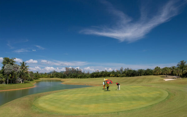 Gruppe golfspillere, der nyder et spil på Mission Hills Phuket Golf Course omgivet af frodige grønne områder.