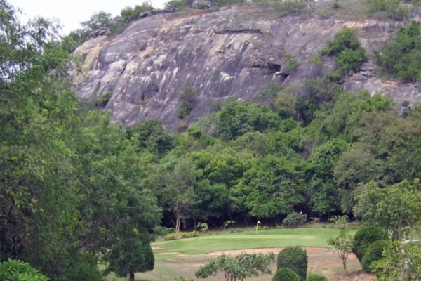 Historisk golfbane i Hua Hin med høje træer og fjern klippeformation