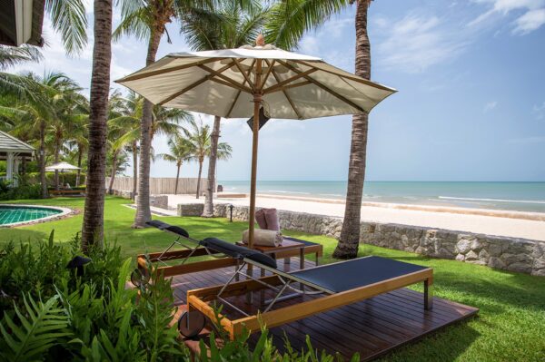 To liggestole under parasol på træterrasse ved Rest Detail Hotel Hua Hin med udsigt til strand, hav og frodig palmelund.