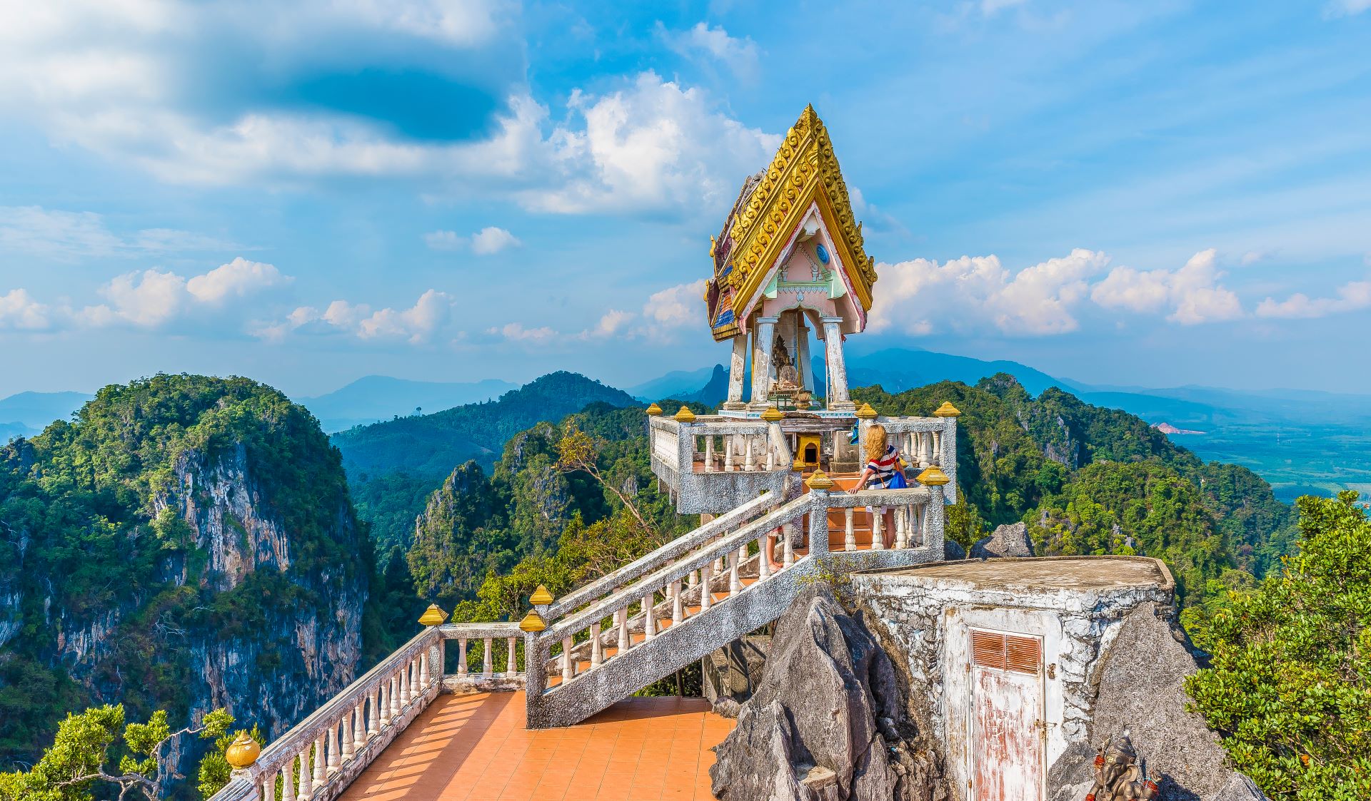 Gyllent tempel med detaljrikt tak på en fjelltopp nær Chiang Mai, omgitt av grønne åser og blålige fjell i horisonten.